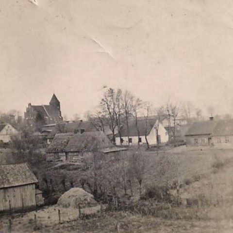 Powiększ obraz: Zdjęcie -  czarno białe zdjęcie przedstawiające historyczną zabudowę wsi Subkowy. W  tle kościół w Subkowach, centralnie położony biały budynek to nieistniejący już subkowski zbór